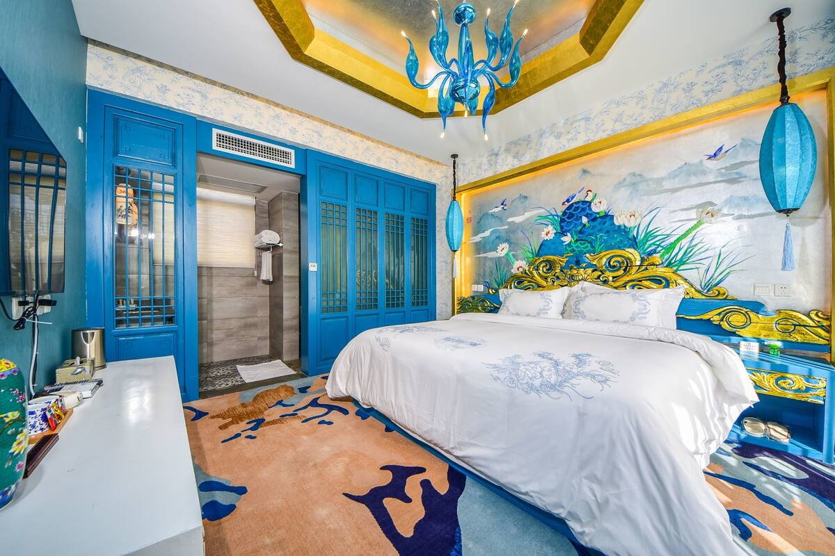 Un dormitorio con una cama grande, un armario azul, un baño con ducha y un mural en la pared.