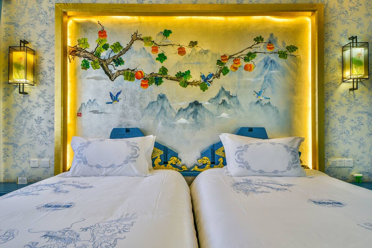 Habitación de hotel con dos camas, un mural decorativo y dos lámparas adosadas a la pared.
