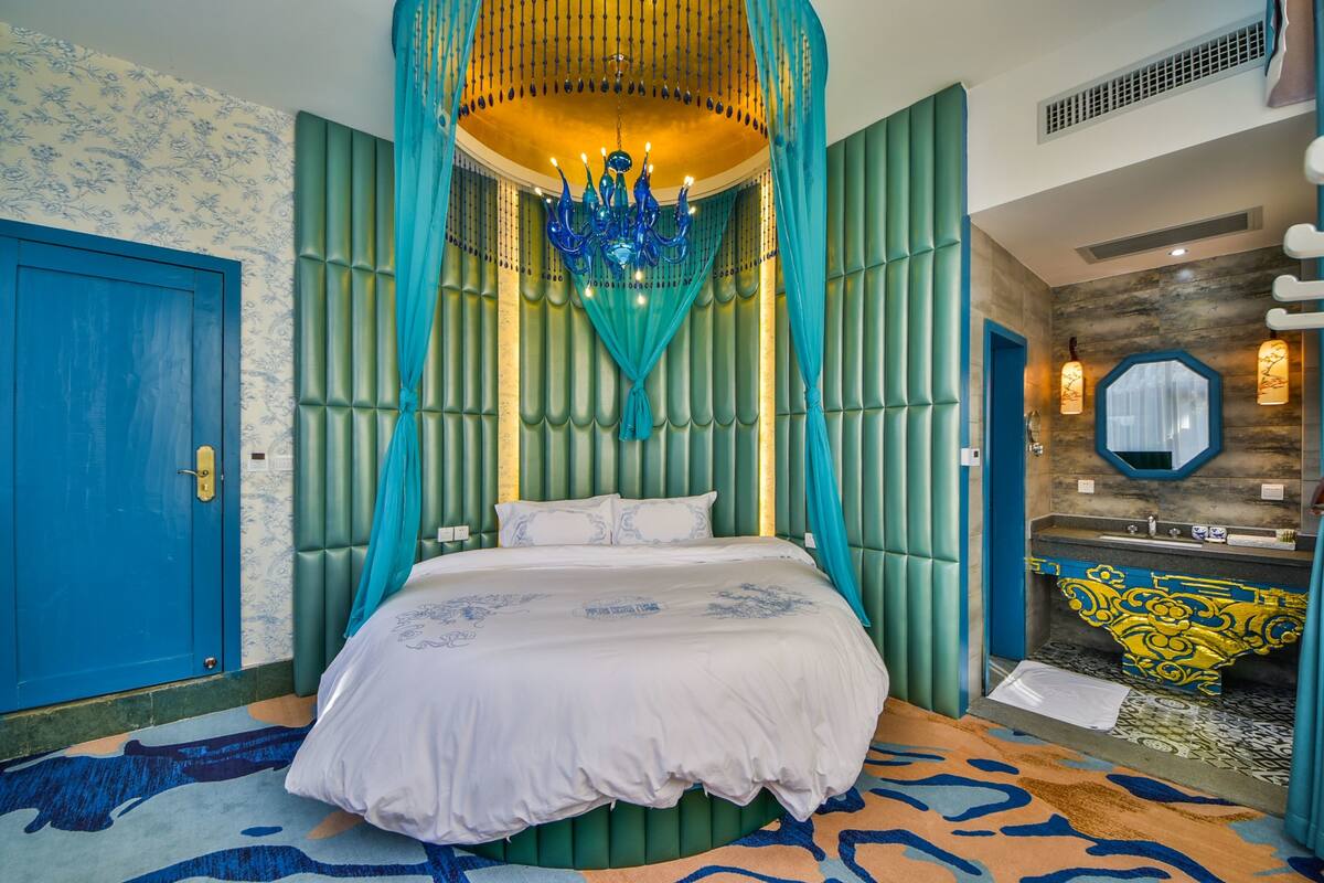 Un dormitorio con cama, un candelabro, un baño con lavabo y espejo, y una alfombra estampada.