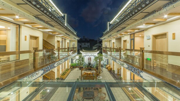 Un vestíbulo de hotel con un patio central, barandillas de vidrio y decoración tradicional.