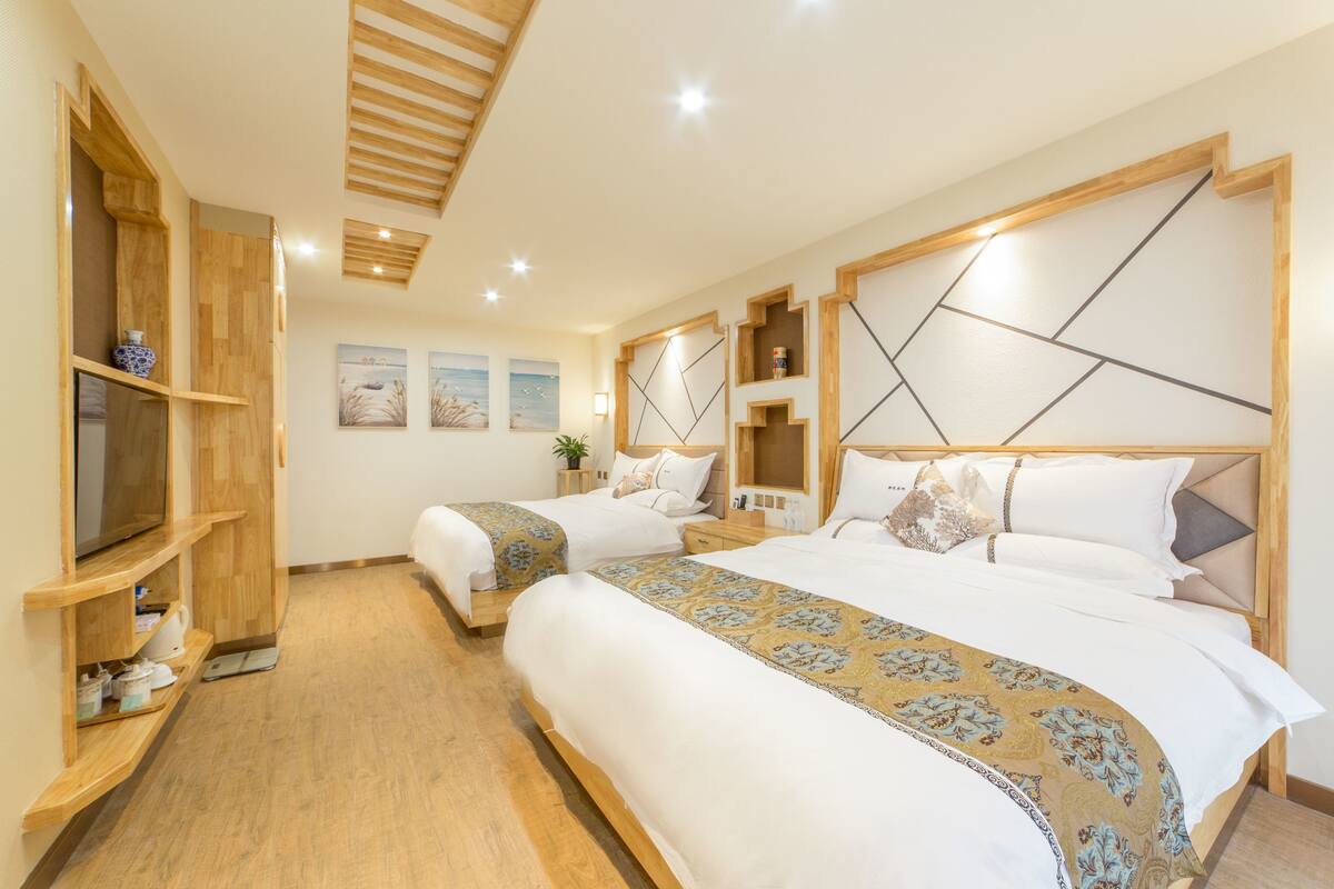 A hotel room with two beds, wooden headboards, a TV, and a wooden shelf with a vase.