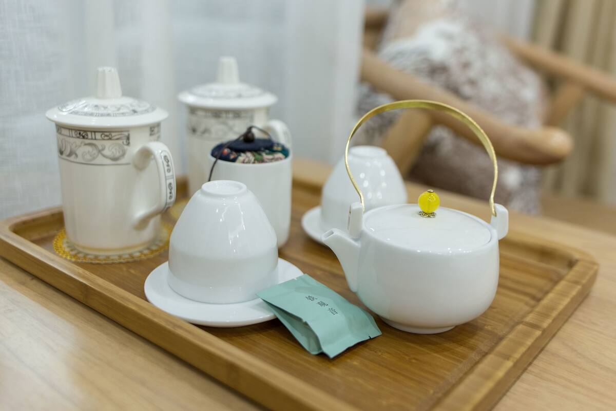 A tray with a teapot, teacups, and a teapot lid on a wooden table.