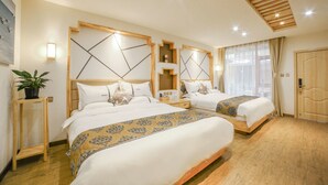 Habitación de hotel con dos camas, cabecero de madera, mesitas de noche, una planta en maceta y un ventanal con cortinas.