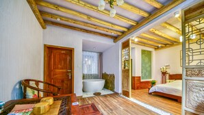 A room with a wooden ceiling, a bathtub, a bed, and a wooden table with a placemat.