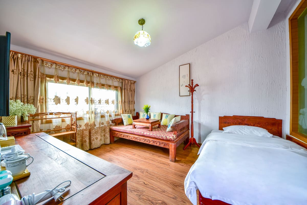 Een kamer met een bed, een houten tafel, een bank en een raam met gordijnen.