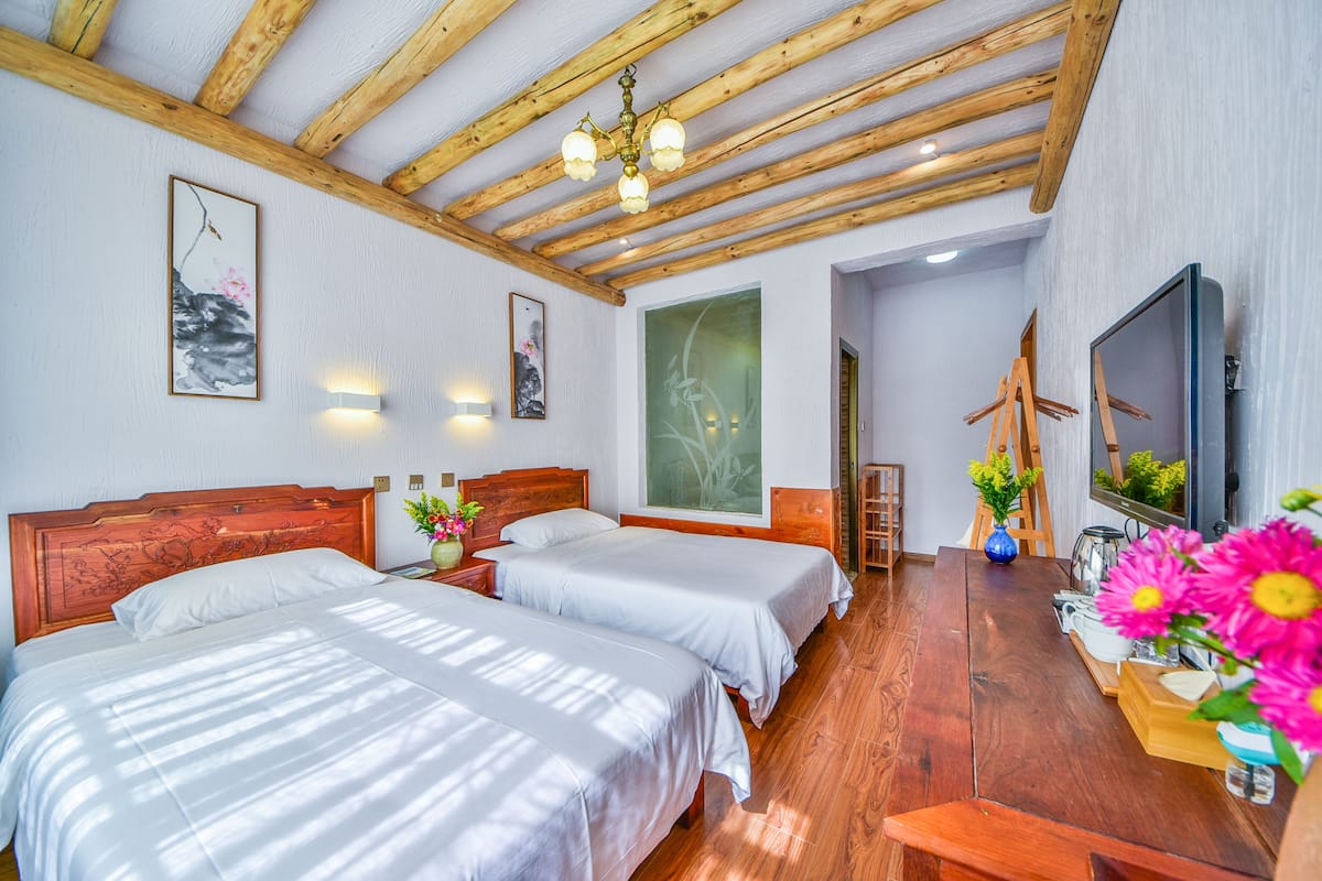 Een hotelkamer met twee bedden, houten balken in het plafond, een groot raam en een houten tafel met bloemen.