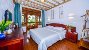 A hotel room with a wooden ceiling, a bed with white linens, a wooden nightstand with a vase of flowers, and a desk with a blue vase and a teapot.