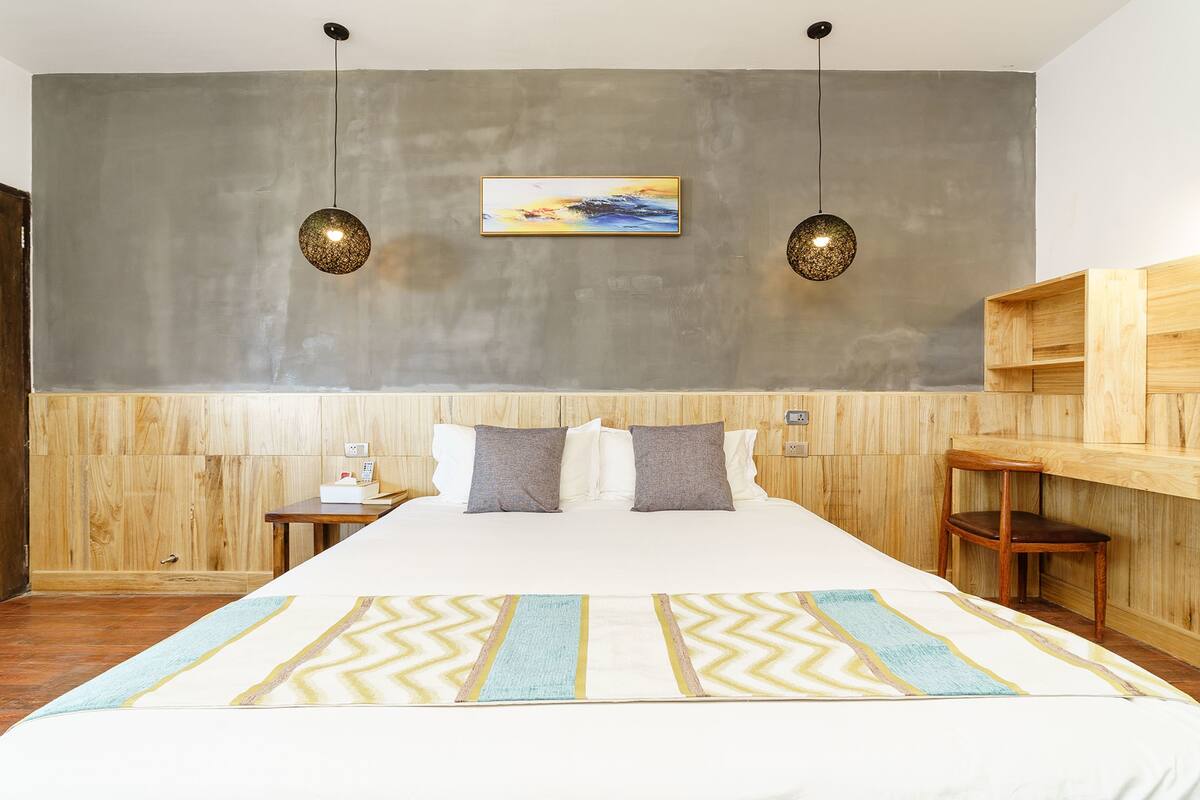 Ein Schlafzimmer mit einem großen Bett, einem Holzkopfstück, zwei Nachttischen, einem Beistelltisch, einem Holzstuhl und einem an der Wand befestigten Regal.