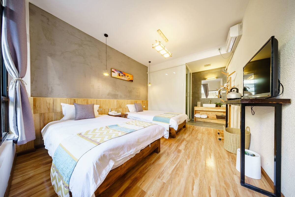 Ein Hotelzimmer mit zwei Betten, Holzboden, einem großen Spiegel und einem durchgehenden Türrahmen erkennbaren Badezimmer.