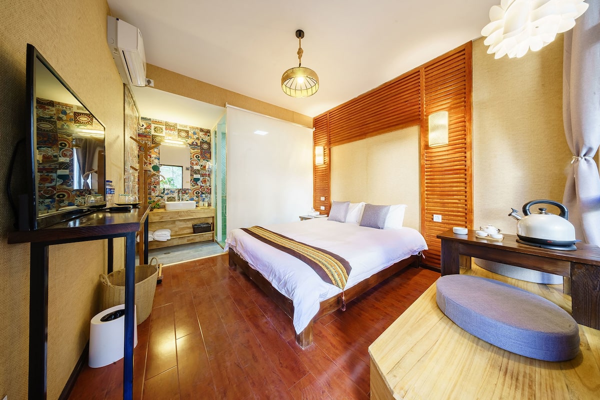 Ein Hotelzimmer mit einem großen Bett, Holzvertäfelung, einem Schreibtisch mit Wasserkocher und einem Spiegel mit farbenfroher Rückwand.
