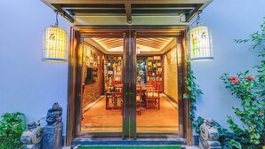 Une entrée de style japonais traditionnel, avec une porte en bois et deux lanternes suspendues. À l’intérieur, on trouve un espace d’accueil avec un comptoir de réception et des chaises.
