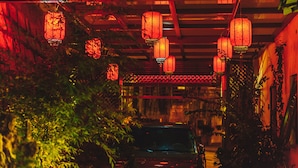 Un couloir décoré de lanternes suspendues, une voiture et un bâtiment présentant des éléments architecturaux traditionnels.