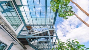 Une structure de verre à plusieurs niveaux, dotée de rampes bleues, qui ressemble probablement à un escalier ou à une plateforme d’observation, entourée de verdure et surplombant un ciel dégagé.