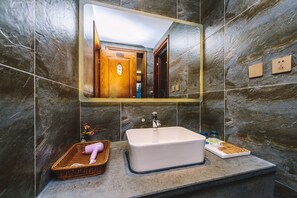 Un baño con un espejo grande, un lavamanos rectangular y una pared de piedra.