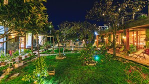 Ein gut beleuchteter Gartenbereich im Freien mit Sitzgelegenheiten, Topfpflanzen und einem Weg zu einem Gebäude.