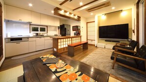 A modern living room with a wooden coffee table, a sofa, a TV, and a kitchen area with a microwave and refrigerator. - Kyotoya Junnya (Kyoto)