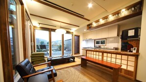 A modern living room with a large window, a wooden bench, and a kitchen area with a microwave and a TV. - Kyotoya Junnya (Kyoto)
