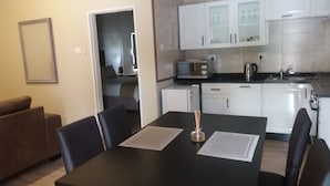 Un espace de vie compact comprenant une table à manger, des chaises, un coin cuisine avec des meubles blancs, un four à micro-ondes et une machine à café.