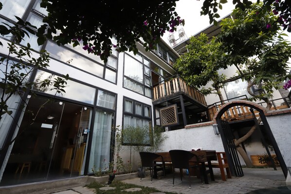 A building with large windows, a wooden balcony, and a garden area with a table and chairs.