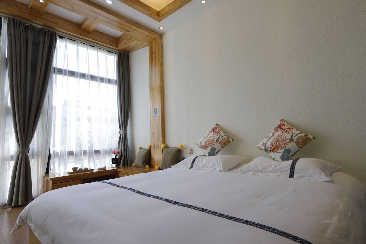 A bedroom with a large bed, wooden headboard, and a window with curtains.