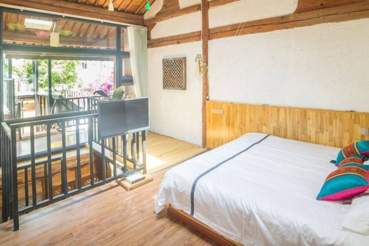 A room with a wooden ceiling, a bed with colorful pillows, a small table, and a window with a view.