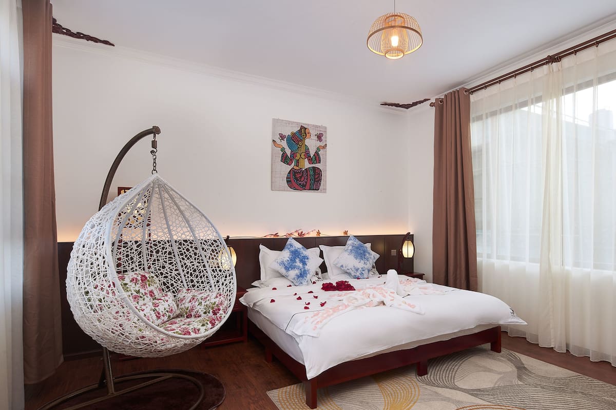 Ein Schlafzimmer mit einem Bett, einem Hängesessel, einem Wandbild und einem großen Fenster mit Vorhängen.