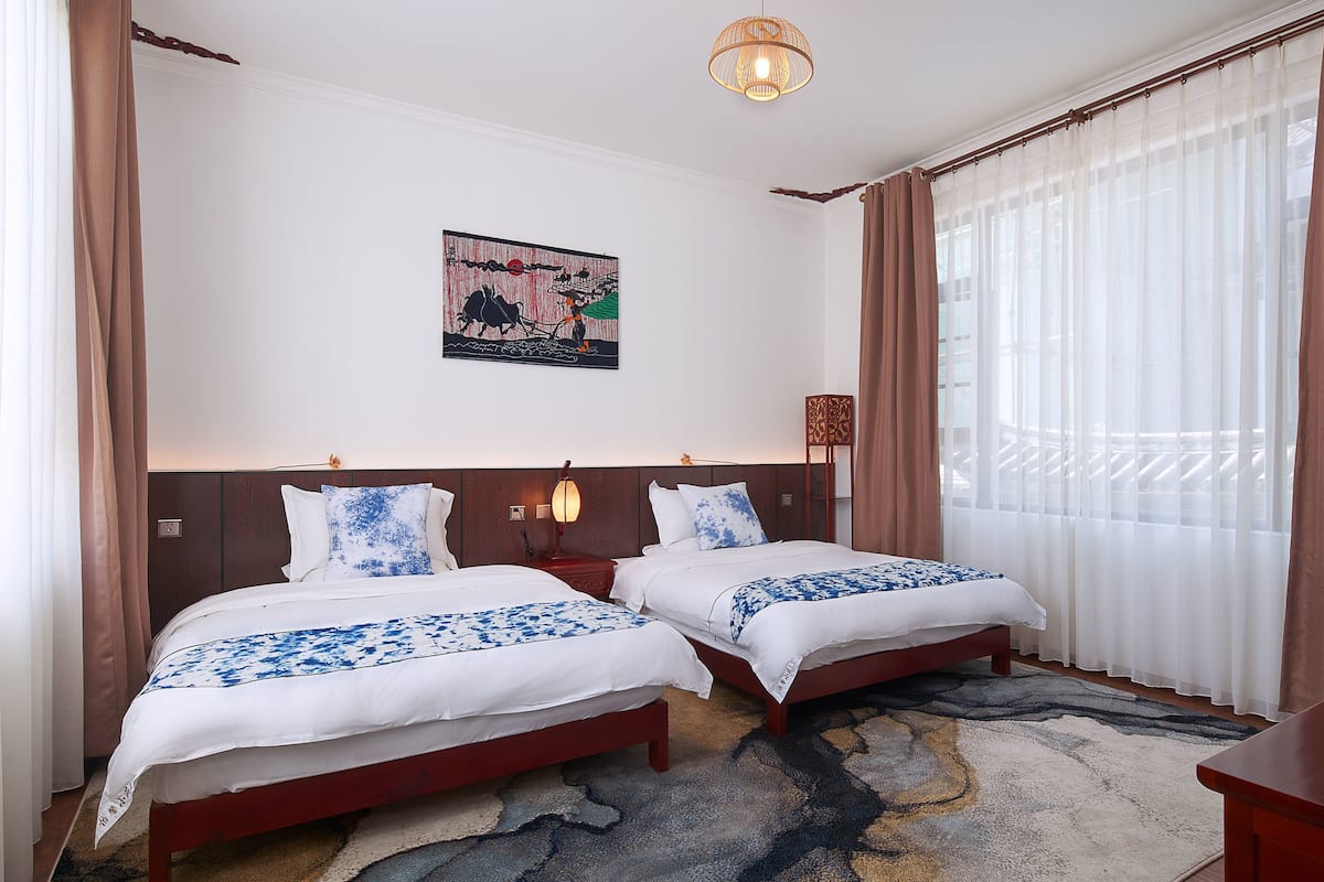 Ein Hotelzimmer mit zwei Betten, einem Fernseher, einem Bild an der Wand und einem großen Fenster mit Vorhängen.
