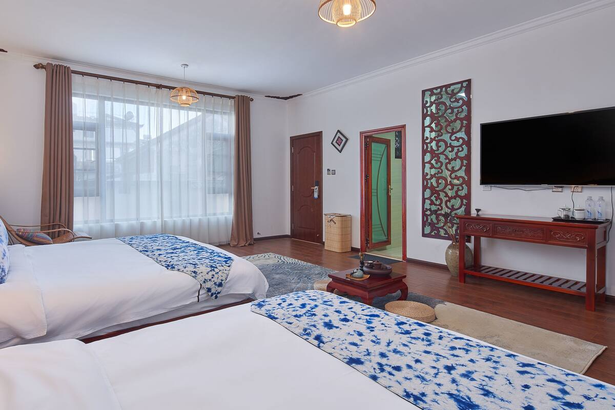 Ein Hotelzimmer mit zwei Betten, einem Fernseher, einem Schreibtisch und einem Fenster mit Vorhängen.