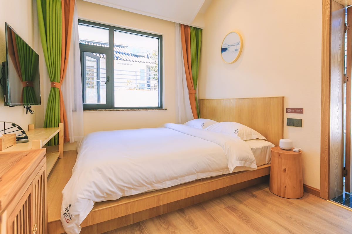 Een hotelkamer met een houten bed, nachtkastje, televisie en een raam met gordijnen.