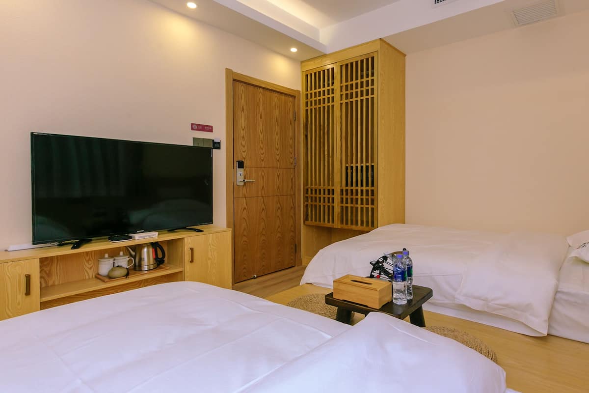 Hotelkamer met twee bedden, een televisie, een houten kledingkast en een klein tafeltje met een fles en glazen.