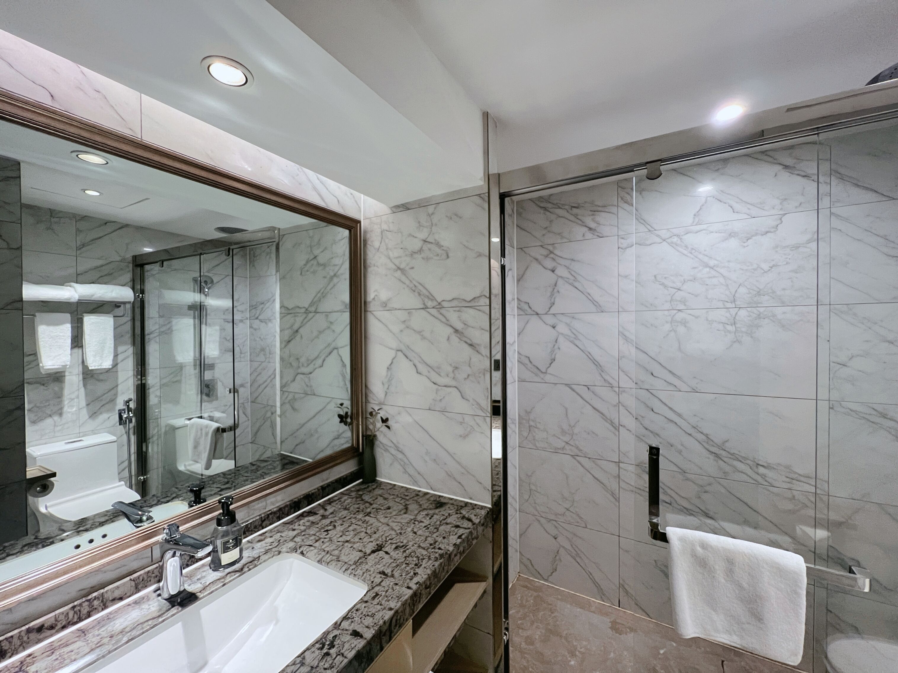 A modern bathroom with a marble vanity, a large mirror, and a glass-enclosed shower.