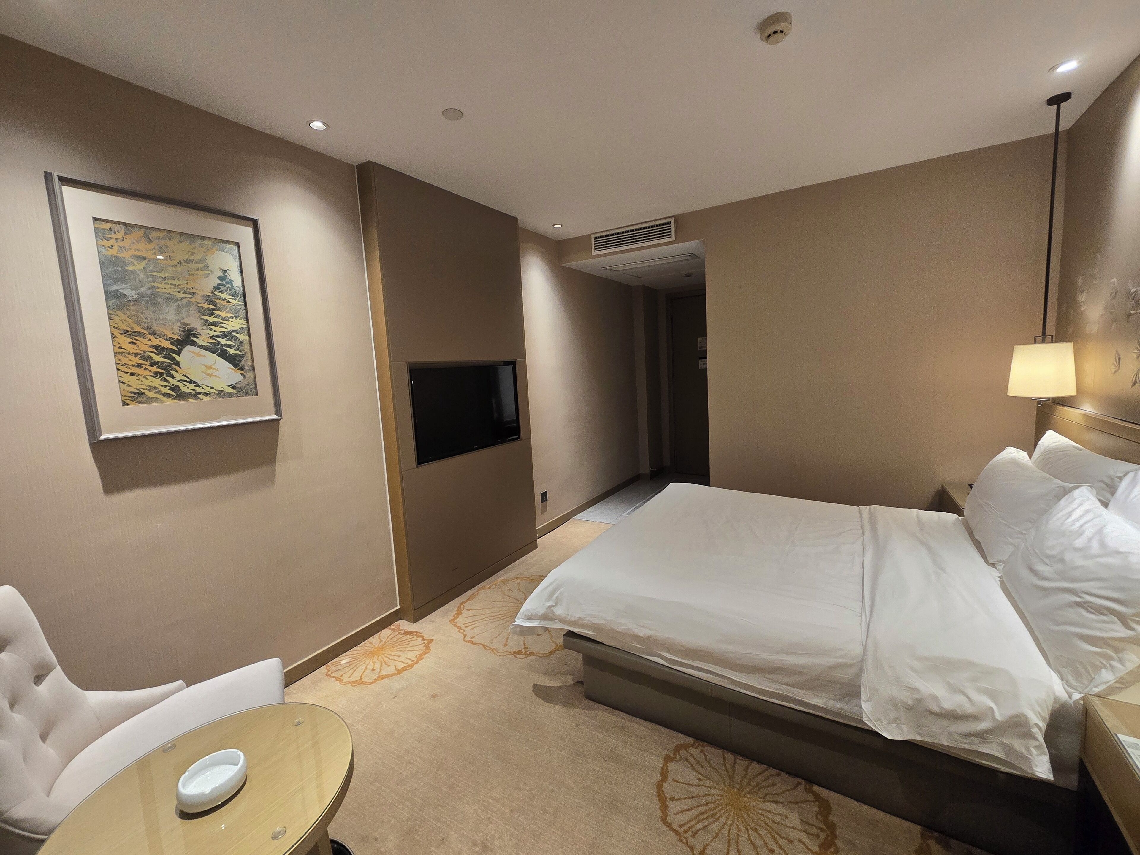 Una habitación de hotel con cama, escritorio, silla, televisión de pantalla plana y un cuadro en la pared.