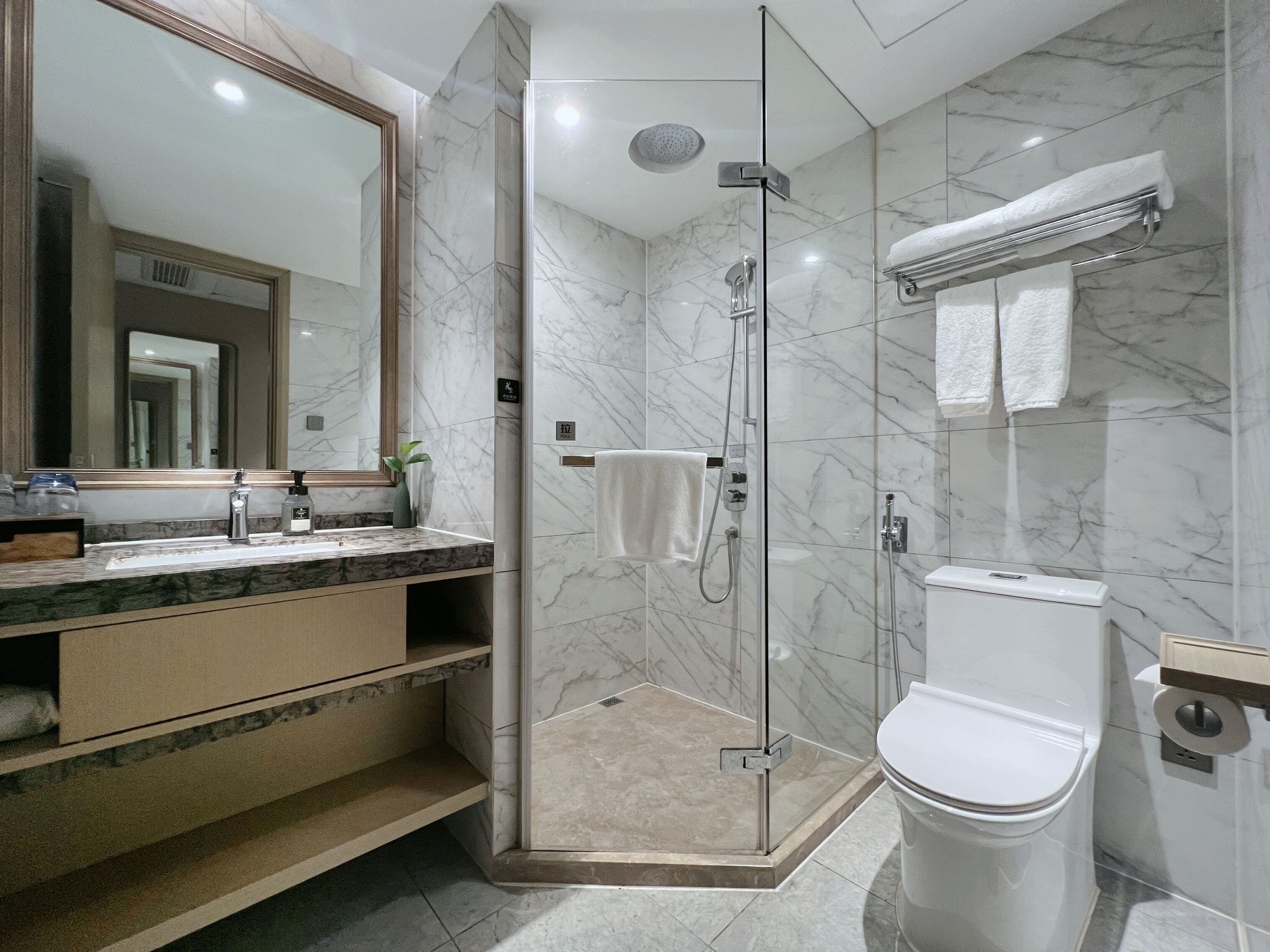 Un baño moderno con ducha de vidrio, inodoro blanco y tocador con azulejos de mármol.