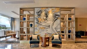 A modern lobby with a marble floor, two armchairs, a large abstract wall art, and a series of shelves with decorative items. - Byland Star Hotel (Jinhua)