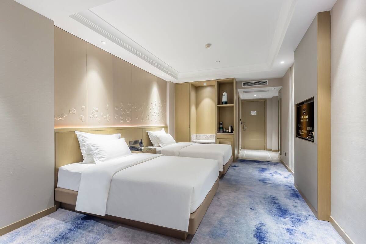 Een hotelkamer met twee bedden, een minibar, een badkamer en een hal met een blauw tapijt.