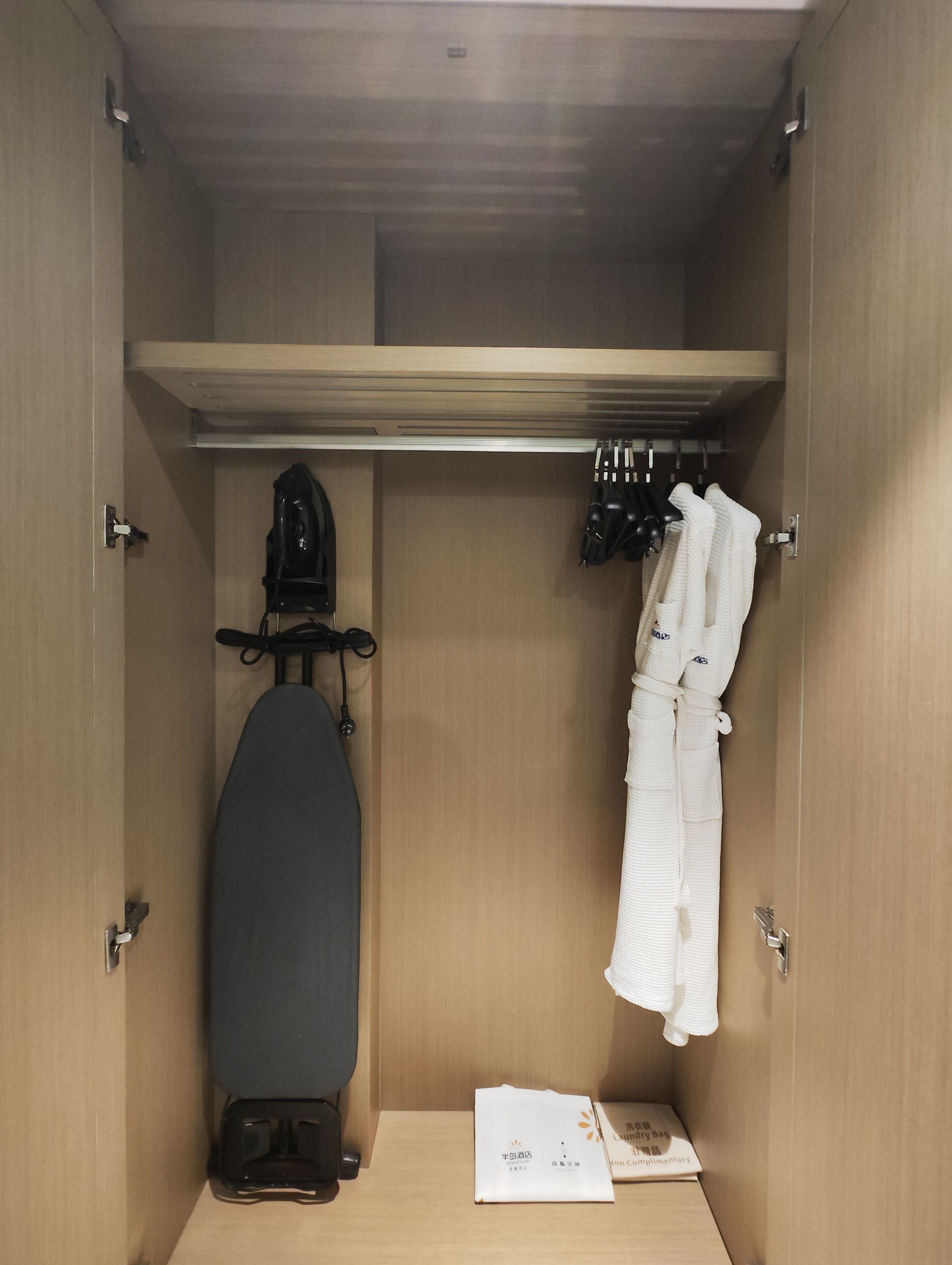 Une petite pièce avec une armoire en bois, une valise noire, une robe blanche et un sac noir.
