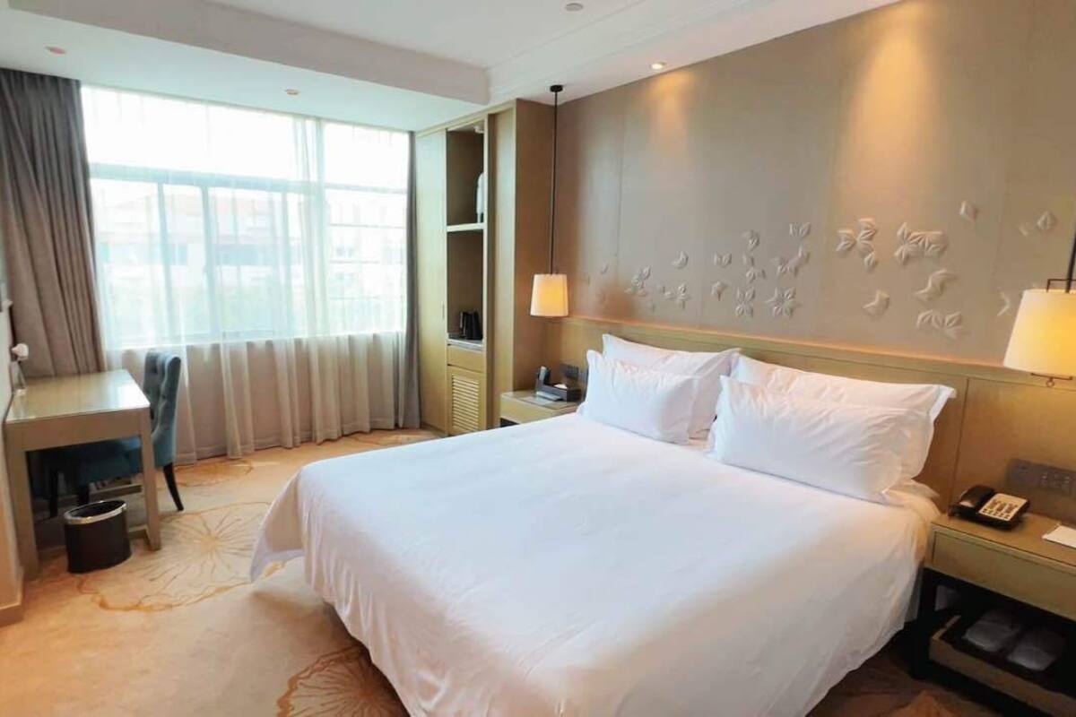 Een hotelkamer met een groot bed, nachtkastjes, een bureau en een raam met gordijnen.
