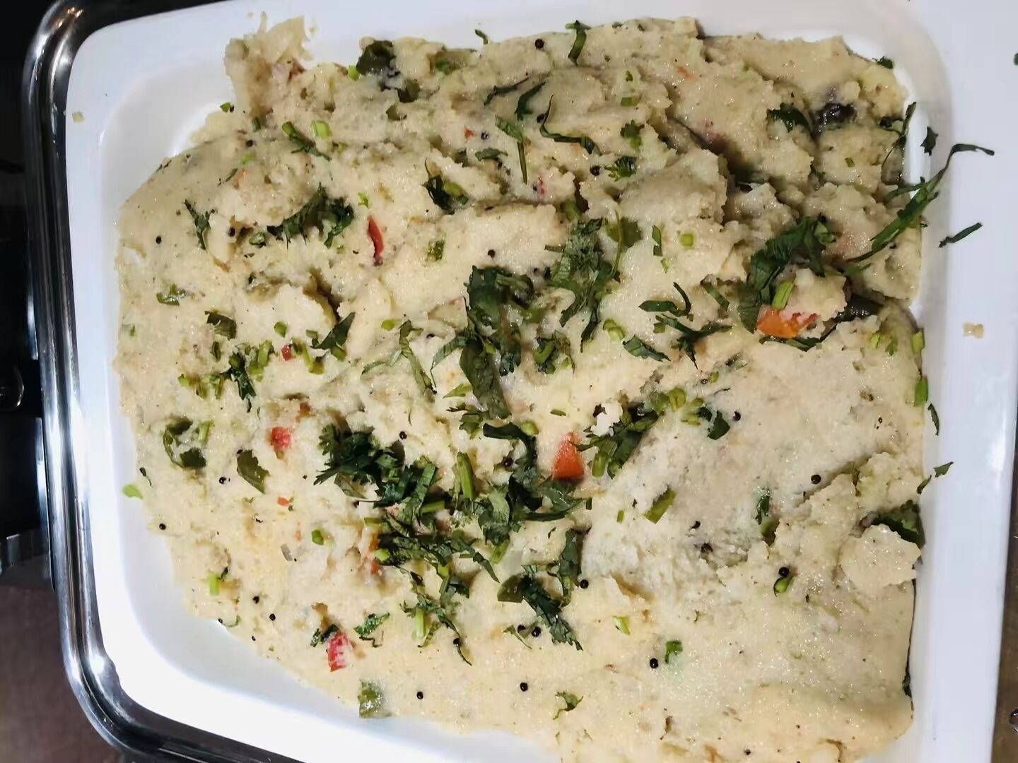 A dish with a creamy texture, garnished with herbs and small bits of vegetables.