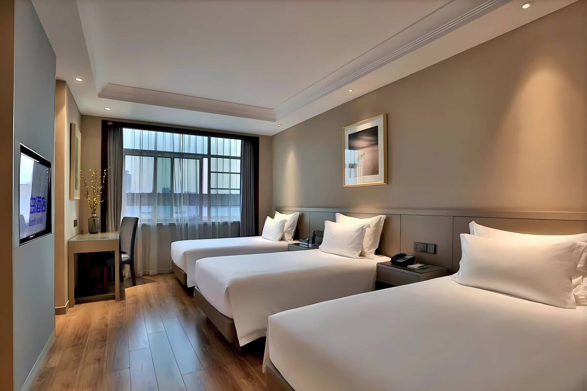 Hotelkamer met twee bedden, een bureau met stoel, een televisie en een raam met gordijnen.