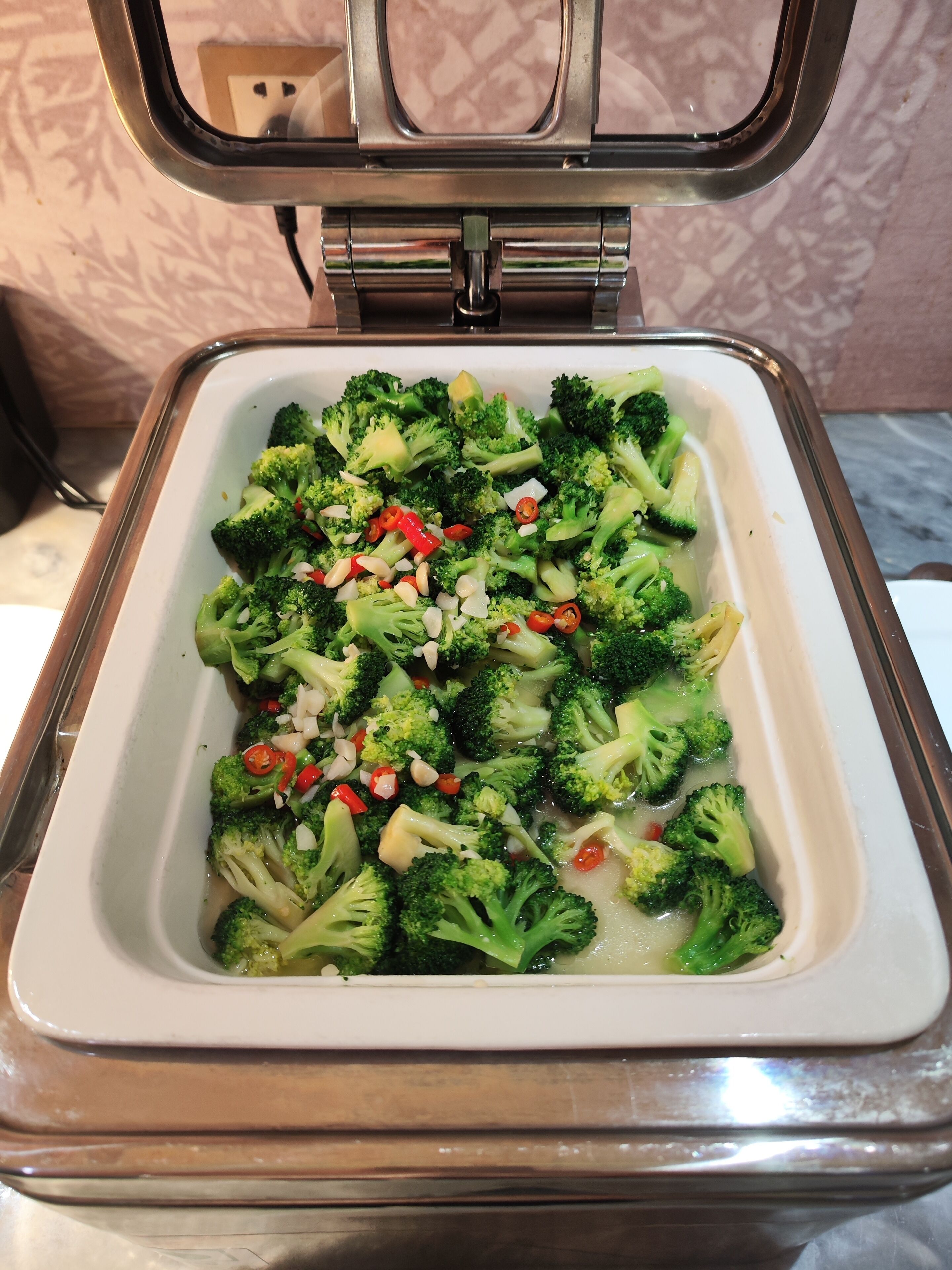 A white rectangular serving dish filled with steamed broccoli and sliced red chili peppers.