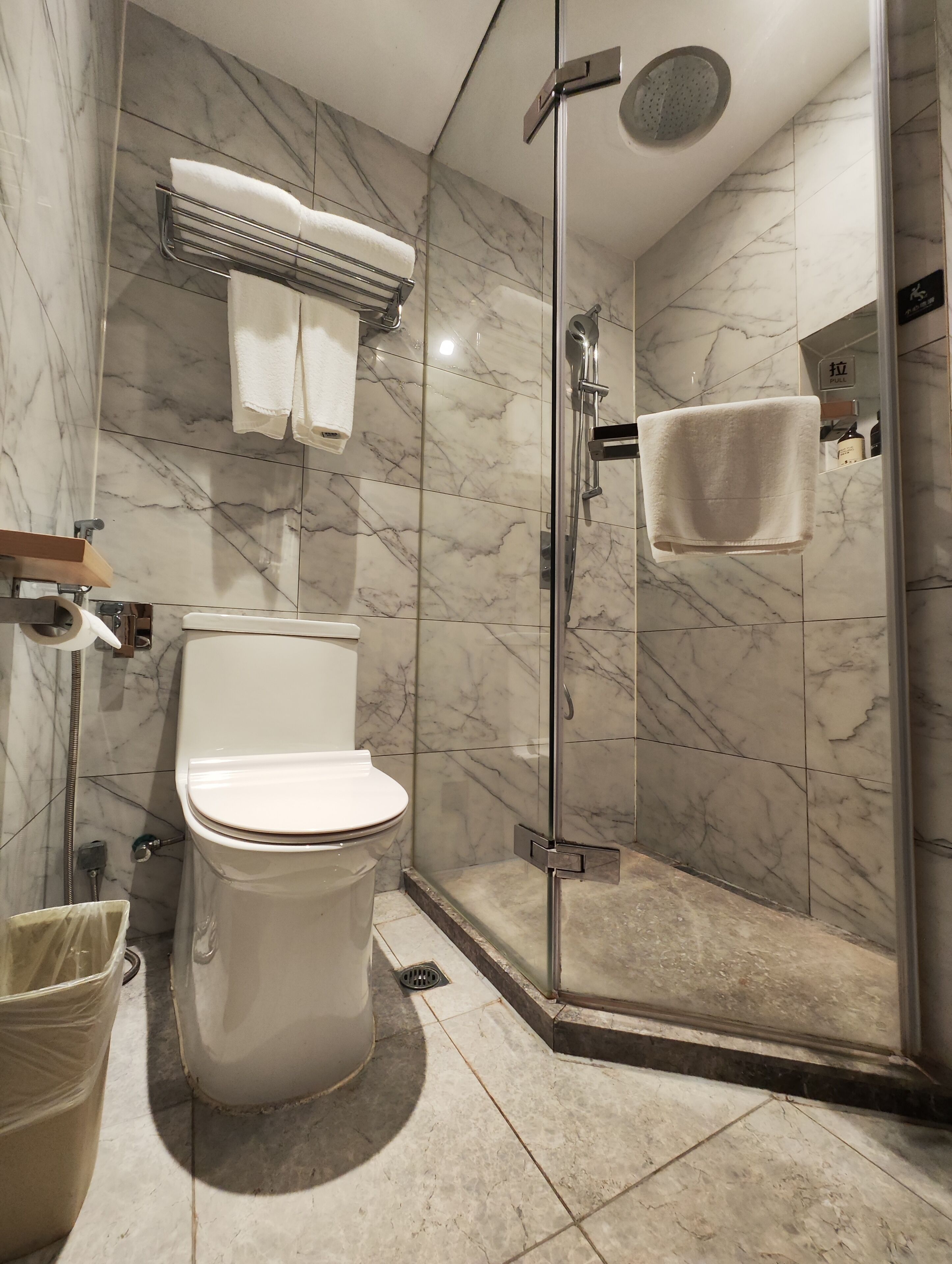 A modern bathroom with a toilet, a glass-enclosed shower, and marble walls.