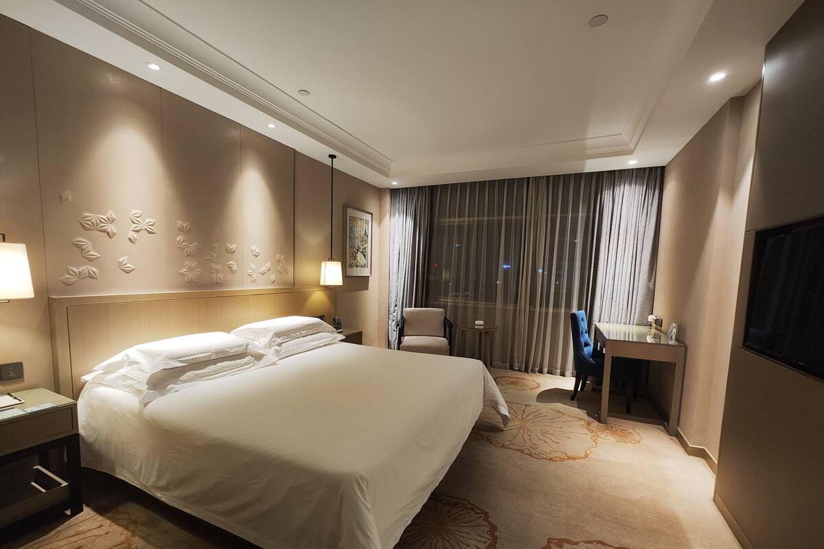 Een hotelkamer met een groot bed, een bureau, een stoel, een lamp en een schilderij aan de muur.