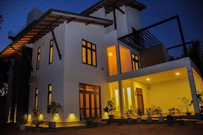 A modern two-story house with a covered porch, multiple windows, and outdoor lighting.