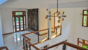 Un interior espacioso con un techo alto, una escalera con barandillas de madera y un moderno candelabro.