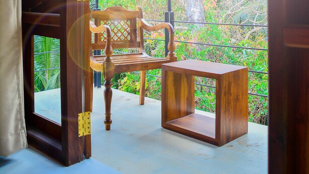 Un balcón de madera con un banco y una mesa, con vista a un jardín exuberante.