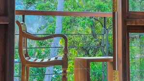 Una silla y una mesa de madera junto a un ventanal con vistas a árboles y un cielo despejado.