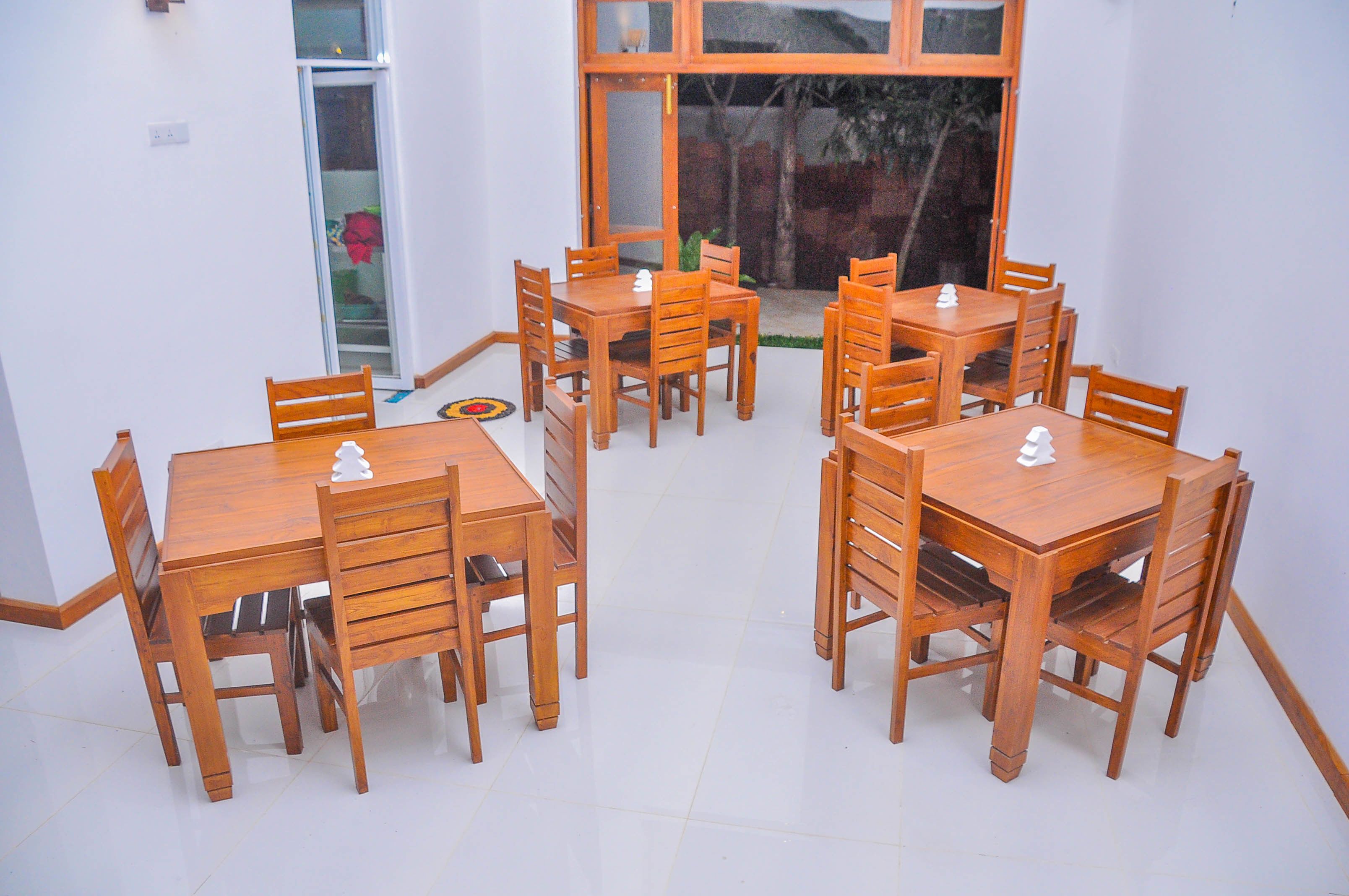 Un espace repas avec des tables et des chaises en bois, une porte-fenêtre coulissante et une vue sur l’extérieur.