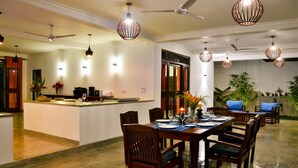 A spacious dining area with a high ceiling, pendant lighting, and a central island with a kitchen counter. - Silence Garden (Hikkaduwa)