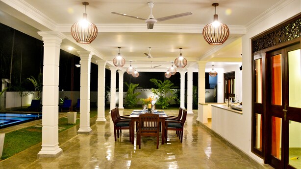 A spacious indoor area with a dining table set for six, surrounded by chairs, and a ceiling fan overhead. - Silence Garden (Hikkaduwa)