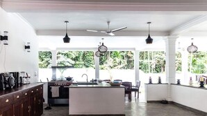 A spacious kitchen with a central island, white cabinetry, and a view of lush greenery outside. - Silence Garden (Hikkaduwa)